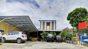 A building with a covered parking area, a blue and yellow facade, and a red flag. - Hotel O Btc Guest House Syariah (Malang)