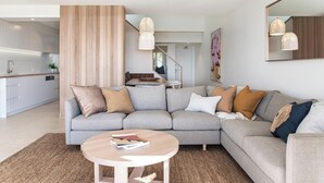 A modern living room with a grey sectional sofa, a round coffee table, and a kitchen in the background.