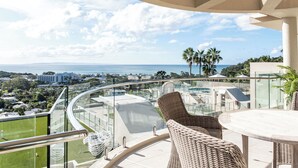 A balcony with wicker furniture, a glass railing, and a view of the ocean and cityscape.