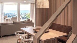 A modern interior with a dining area, a staircase, and a large window offering a view of the ocean.