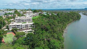 A residential area with modern multi-story buildings, a tennis court, and a river.