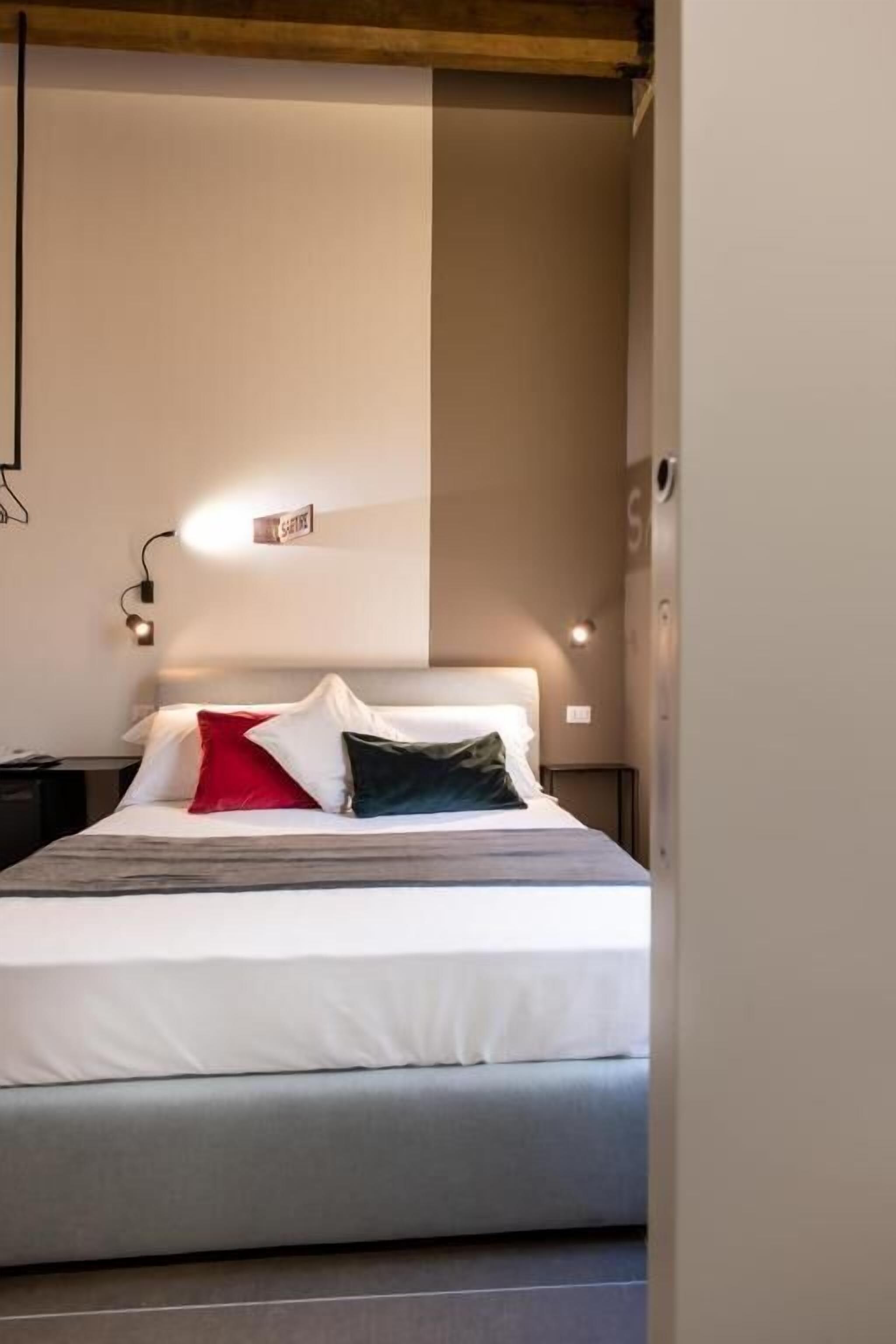 Une chambre d’hôtel moderne, équipée d’un lit, de tables de chevet et d’un luminaire fixé au mur.