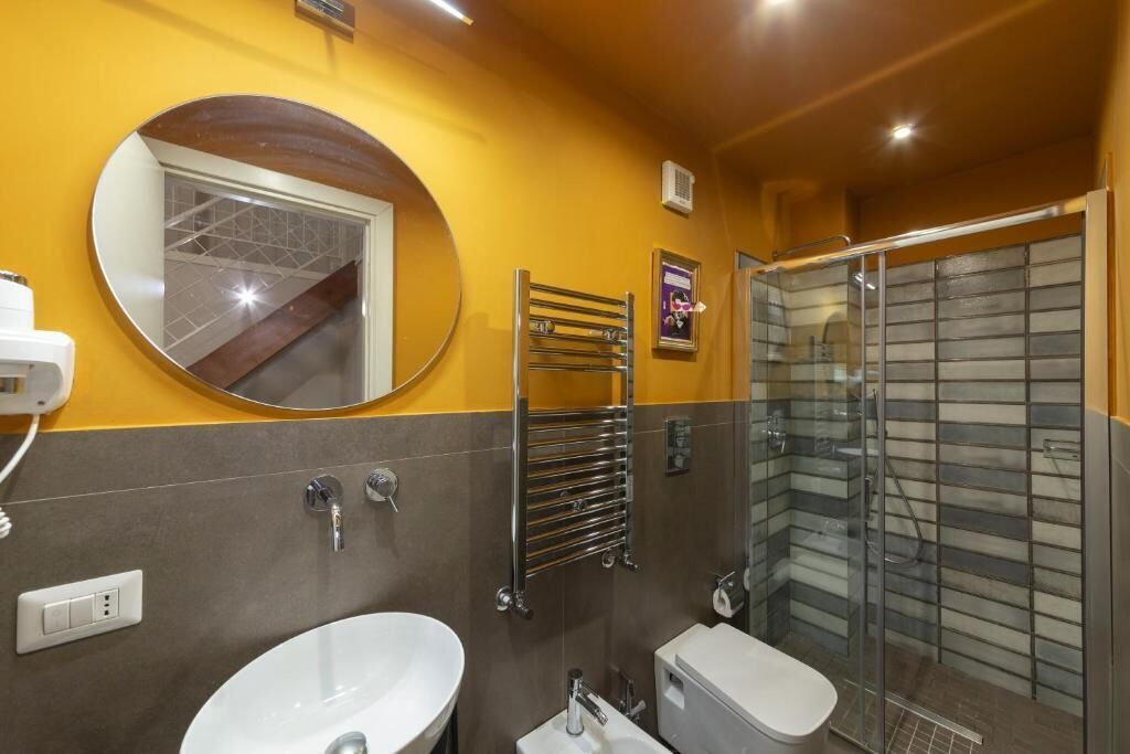 Un baño con espejo redondo, lavabo, inodoro y ducha con cerramiento de vidrio.