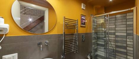 Un baño con espejo redondo, lavabo, inodoro y ducha con cerramiento de vidrio.