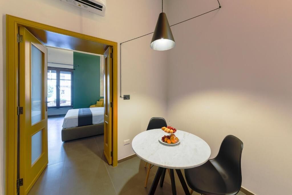 A room with a bed, a dining table with chairs, and a pendant light.