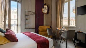 A hotel room with a bed, a small table with a chair, a TV, and a view of the city through the window. - Mastropasqua BB (Naples)