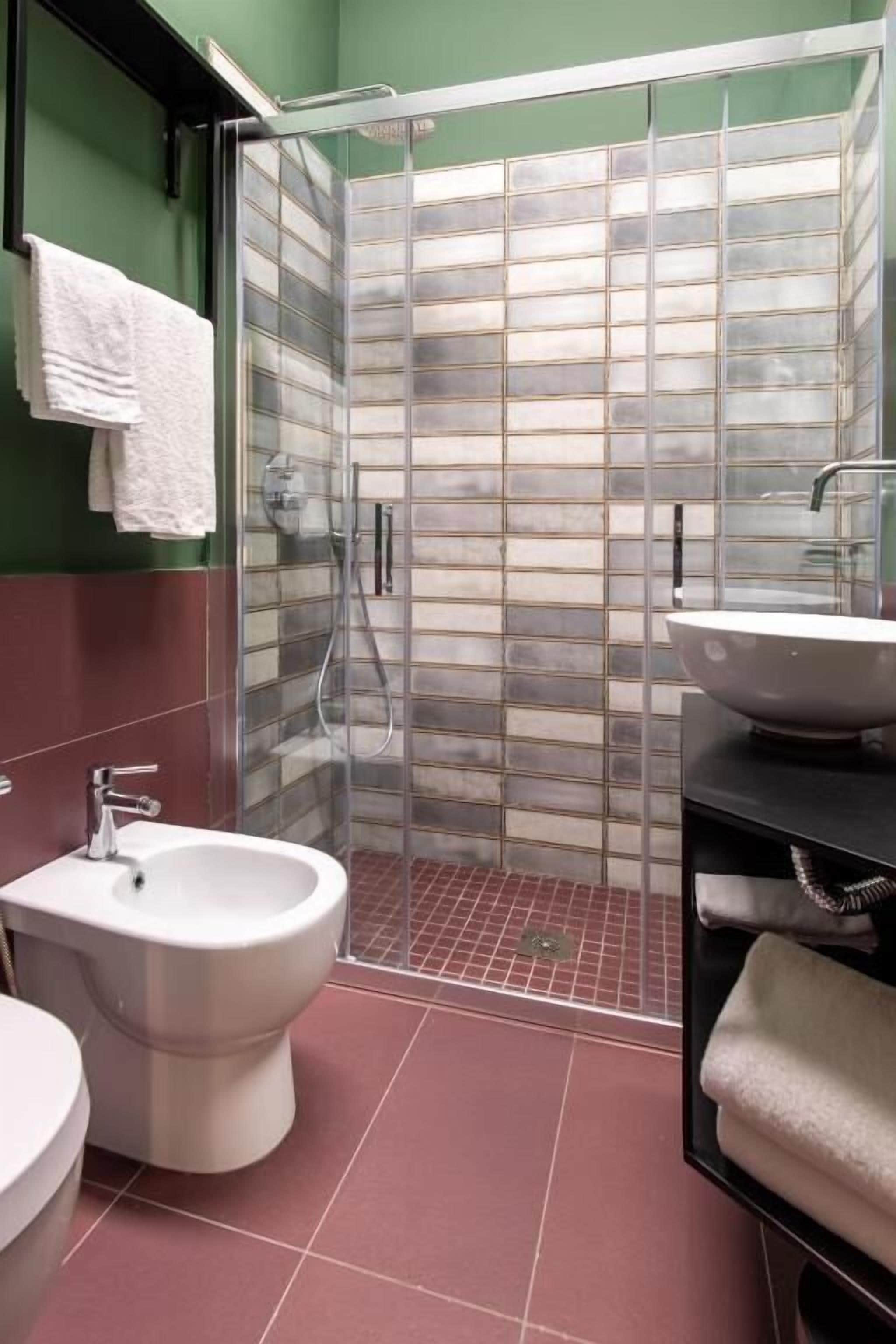 A bathroom with a glass-enclosed shower, a white sink, and a bidet.