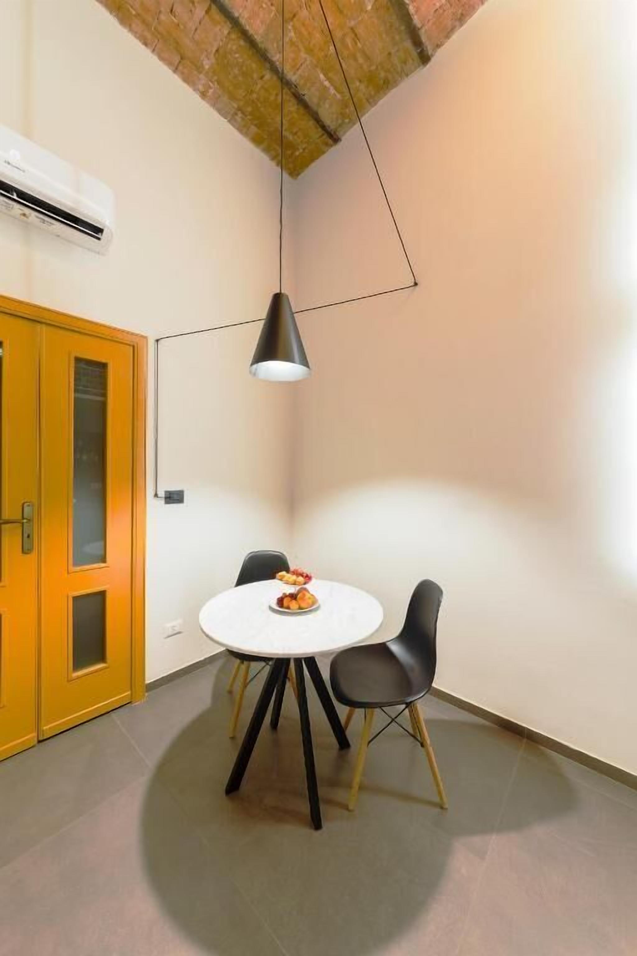 A dining area with a round table, two chairs, a pendant light, and a yellow door.