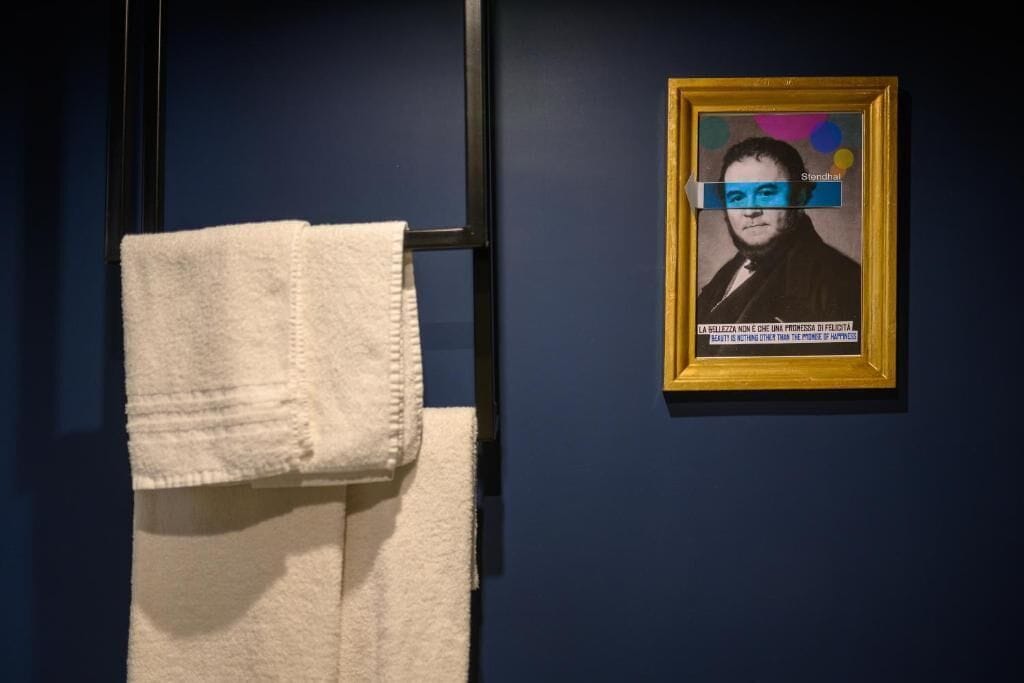A framed portrait on a dark wall, a white towel hanging on a rack, and a black metal structure.