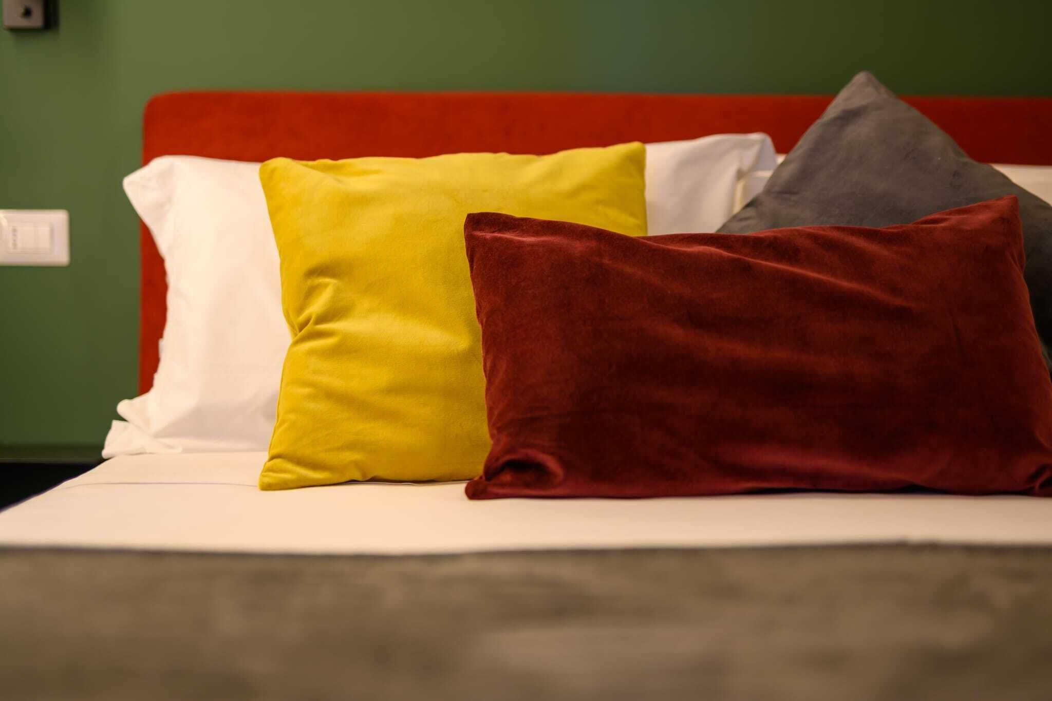A bed with three pillows in different colors.