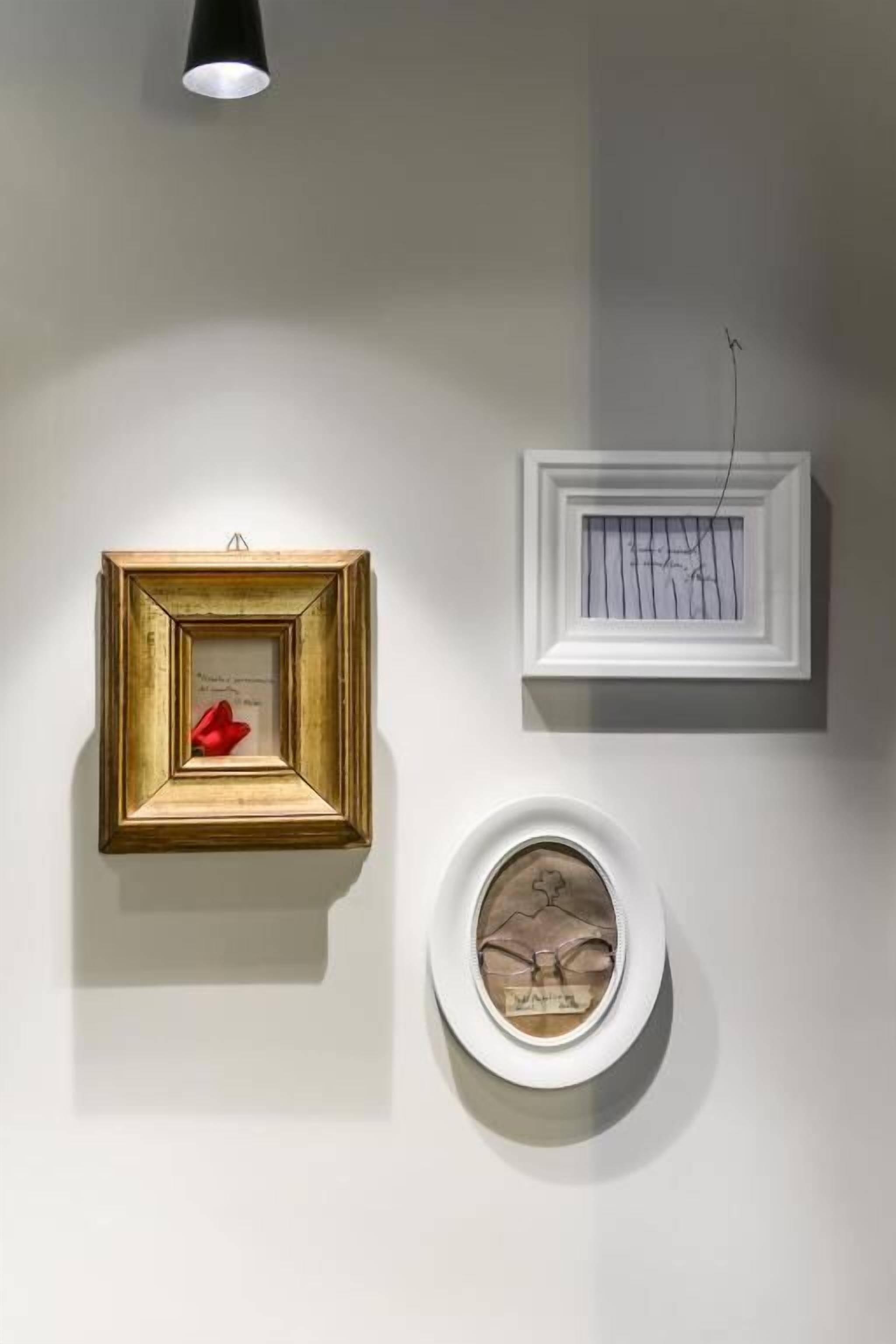 Three framed artworks on a wall, each with different framing styles and a single light source above.