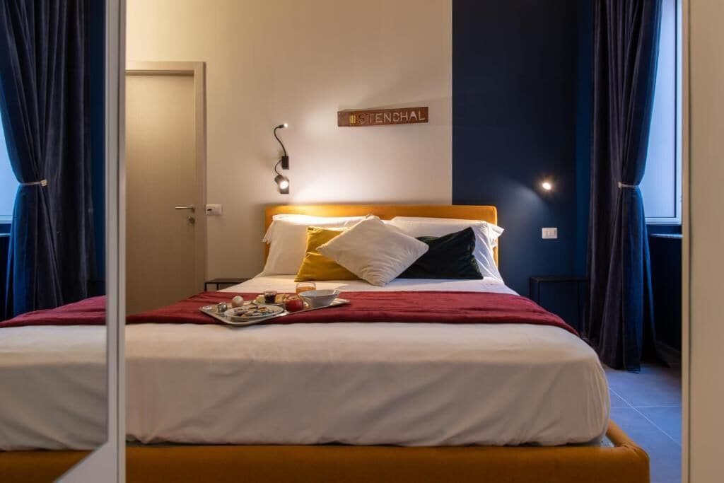 Een net opgemaakt bed met een rode deken, witte kussens en een bord op de muur waarop 'MISTENCHAL' staat.