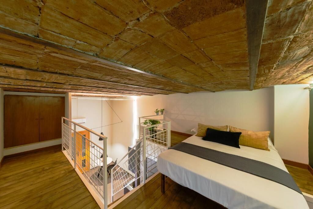 A bedroom with a wooden ceiling, a bed with white bedding, and a staircase leading to an upper level.