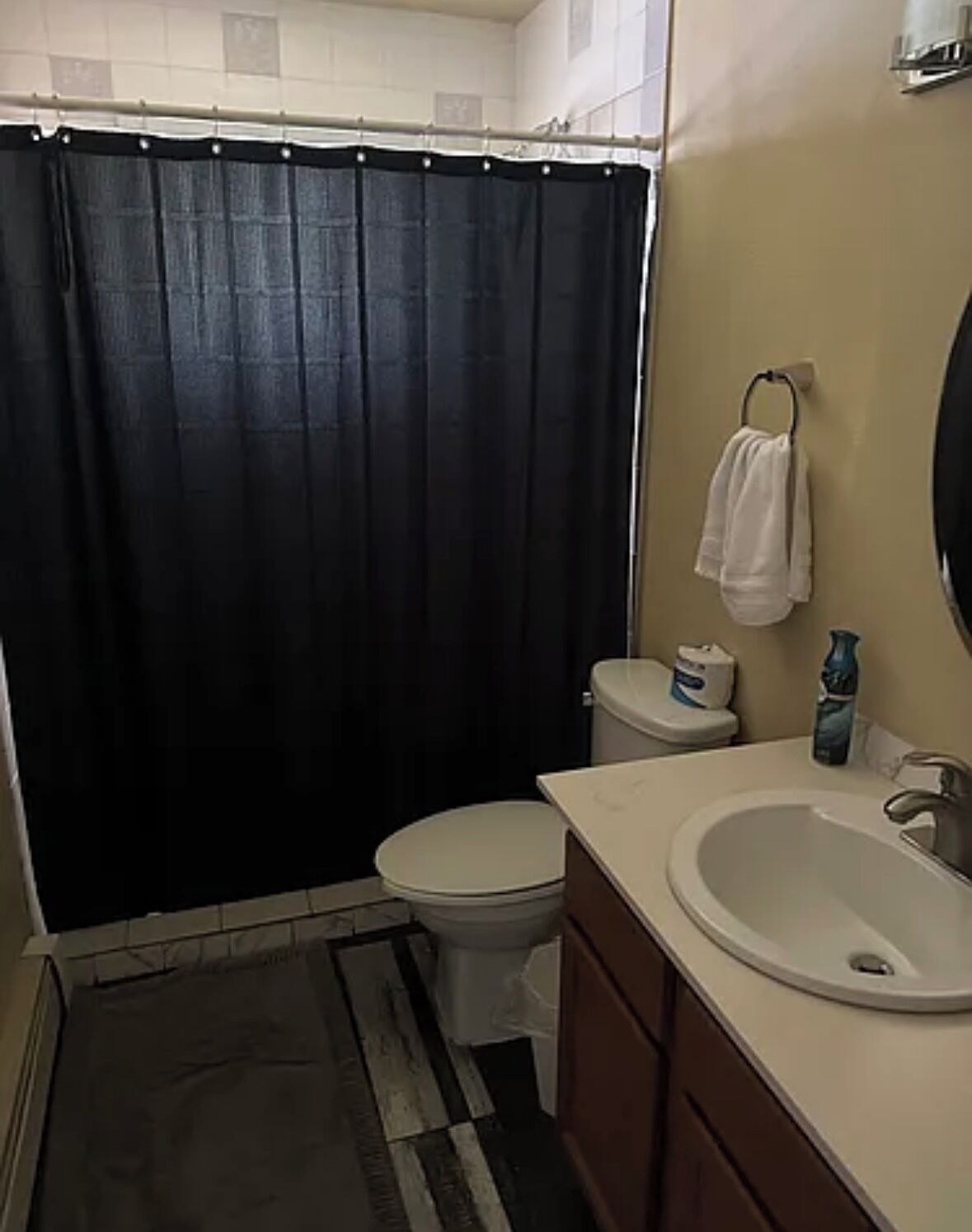A bathroom with a black shower curtain, a white toilet, a sink with a mirror, and a towel hanging on the wall.