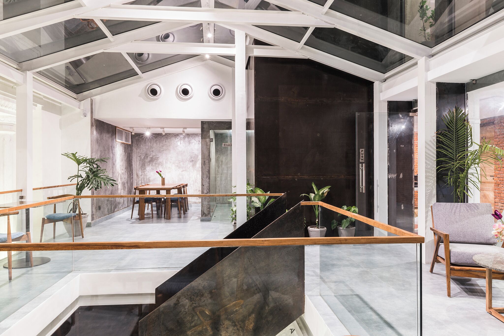 A modern interior with a glass staircase, a dining area, and a seating area with plants.
