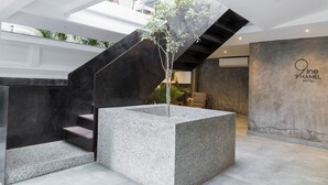 A modern hotel lobby with a central staircase, a concrete planter with a tree, and a large wall with the hotel name. - 9ine Thamel Hotel (Kathmandu)