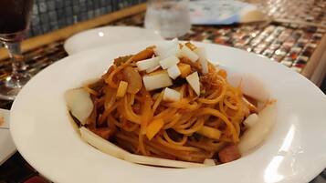 A plate of spaghetti with vegetables and meat, a glass of water, and a wine glass on a table with a tiled pattern.