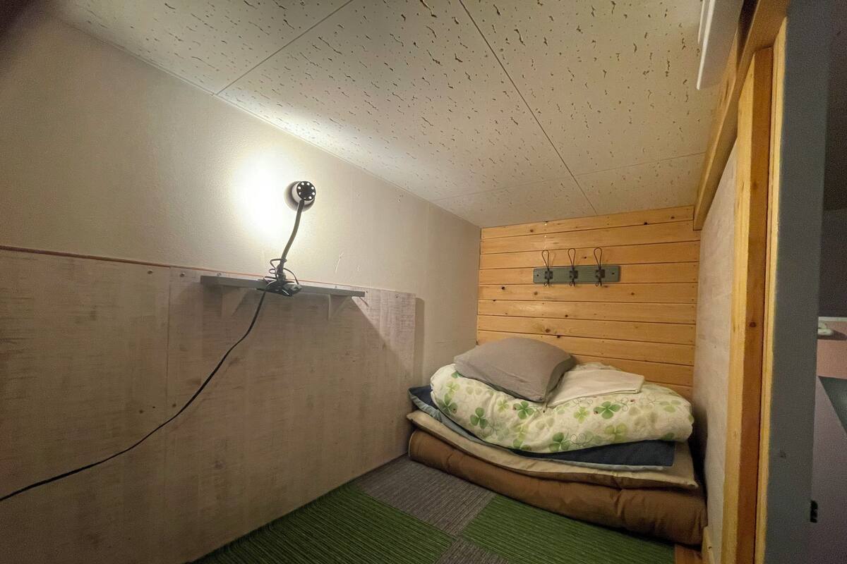 Una habitación pequeña y acogedora con techo inclinado, una cama individual con almohada, una lámpara de pared y un revestimiento de pared de madera.