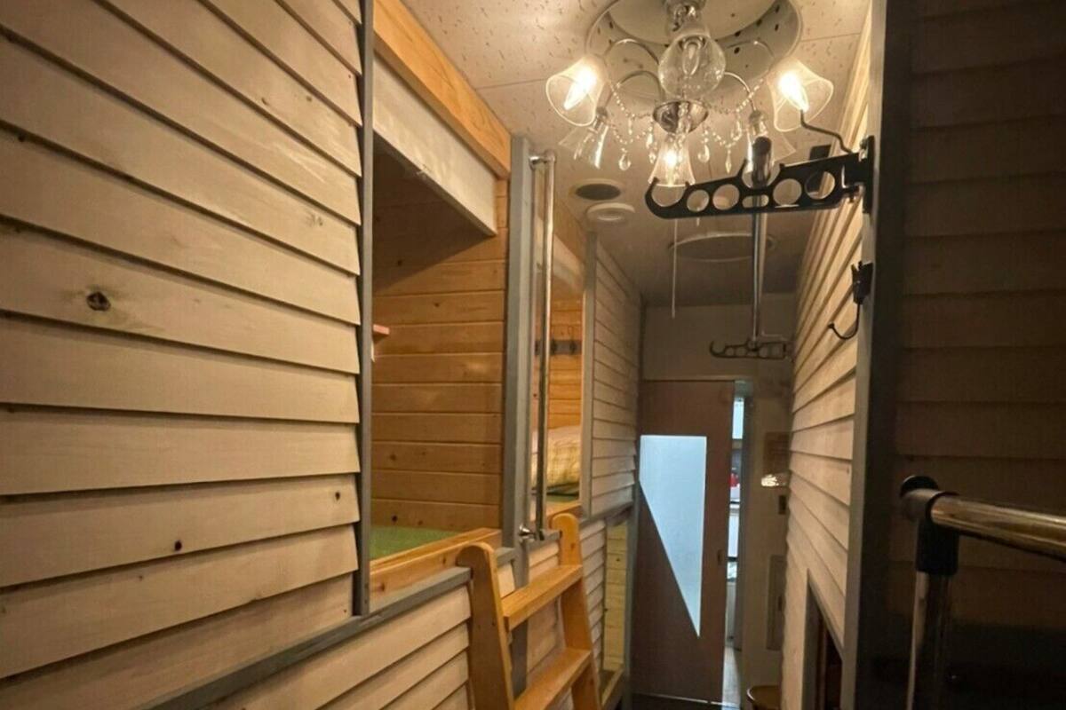 Un estrecho pasillo de madera con una escalera de madera, un aplique de techo y una puerta al final.