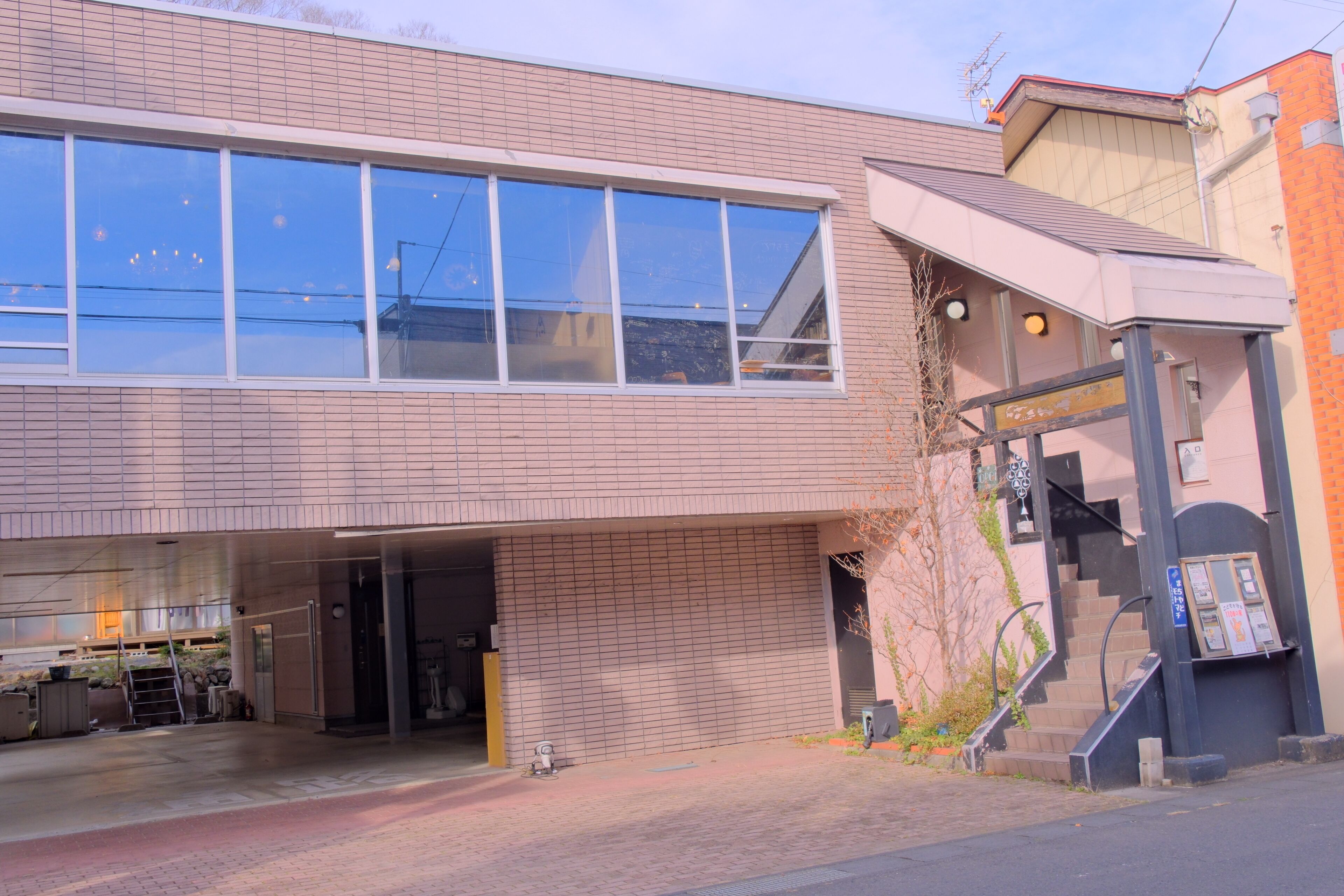 A building with a large window, a covered entrance, and a staircase leading to an upper level.