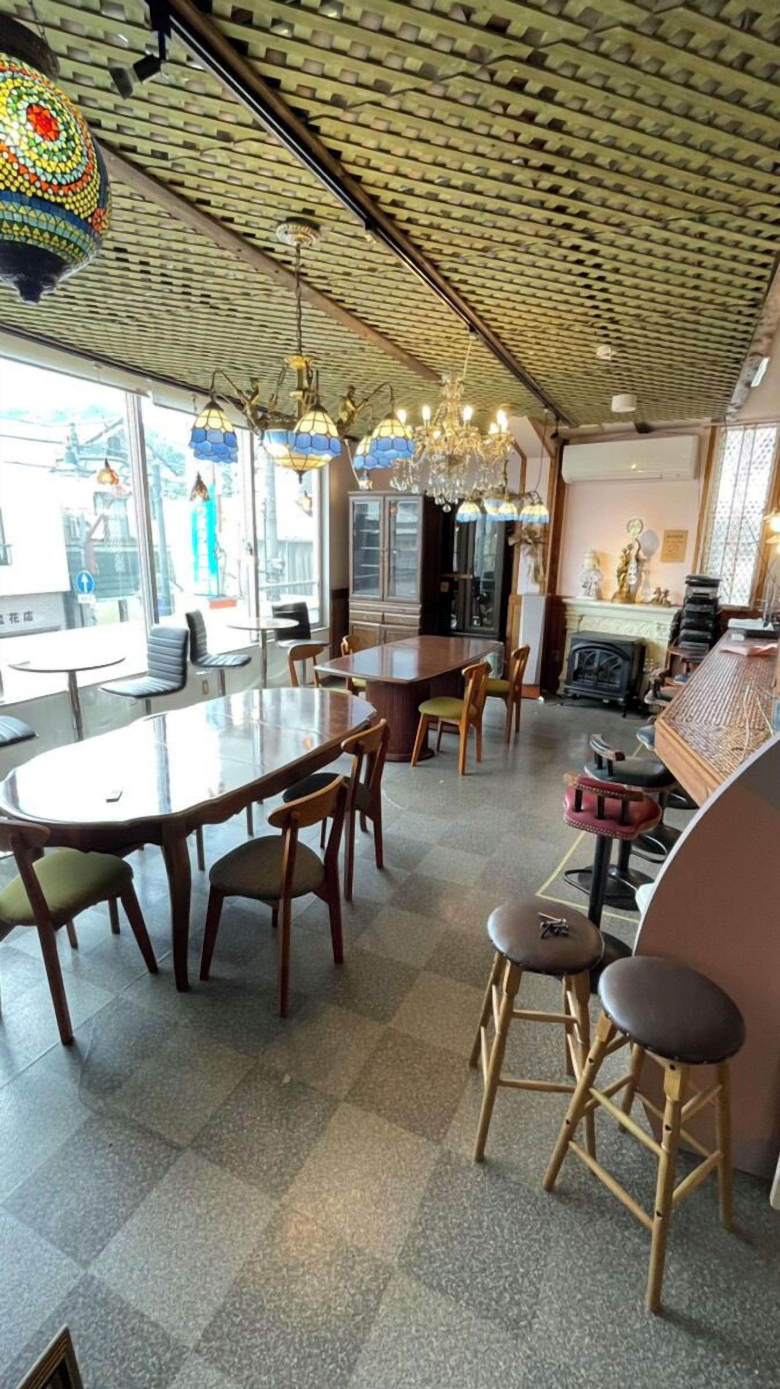 Ein Restaurant mit hoher, gemusterter Decke und verschiedenen hängenden Leuchten. Es gibt mehrere Tische und Stühle, einen Barbereich und einen Kamin.