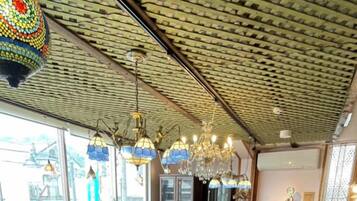 Ein Restaurant mit hoher, gemusterter Decke und verschiedenen hängenden Leuchten. Es gibt mehrere Tische und Stühle, einen Barbereich und einen Kamin.