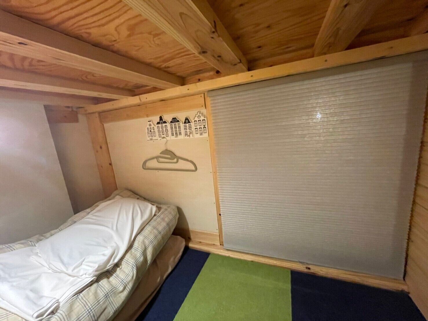 A small, single-bed room with a wooden ceiling and a sliding door.