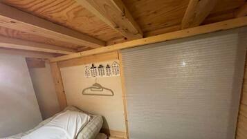 A small, single-bed room with a wooden ceiling and a sliding door.