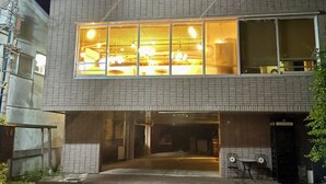 Un bâtiment à deux étages, doté d’une grande fenêtre illuminée à l’étage supérieur, d’une cabine téléphonique bien visible et d’une entrée fermée par un portail.