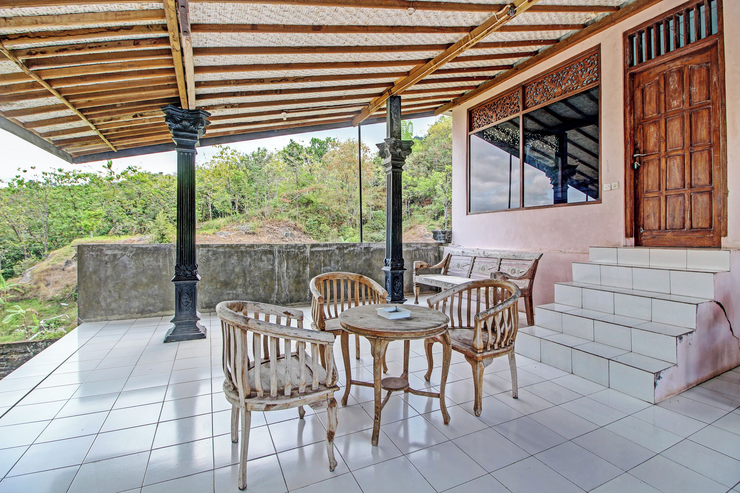 Un patio al aire libre con una pérgola de madera, muebles de mimbre y vistas a la vegetación circundante.