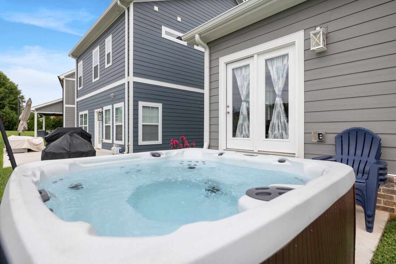 A hot tub in front of a house with a covered patio and a blue chair.
