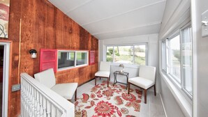 A sunlit room with a wooden wall, white furniture, and large windows. - Hobbit House one of a kind home (Bel Air)