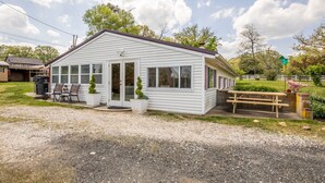 A single-story white building with a gabled roof, a front porch with a bench, and a small garden area with a wooden picnic table. - Hobbit House one of a kind home (Bel Air)