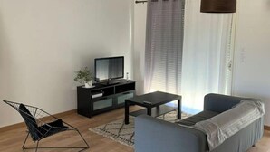 Un salon moderne avec un canapé gris, un meuble de rangement noir et un fauteuil au design original, dont l’armature est faite de fil métallique.