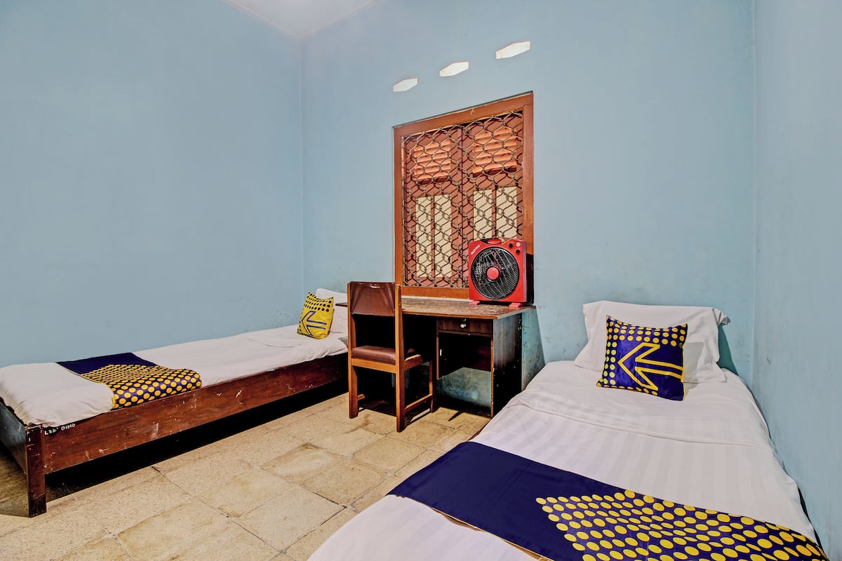 A room with two single beds, a desk with a chair, a fan, and a decorative screen.