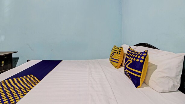 A bed with a white and blue bedspread, two pillows with yellow and blue patterns, and a dark-colored headboard. - SPOT ON 92763 Hotel Melati Sukoasih (Wonogiri)