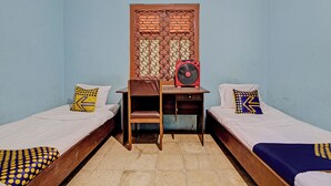 Ein Zimmer mit zwei Einzelbetten, einem Schreibtisch mit Stuhl, einem Ventilator und einer Wandverkleidung.