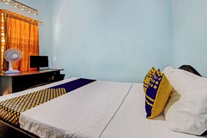 A hotel room with a bed, a desk, a chair, a desk lamp, a monitor, and a standing fan. - SPOT ON 92763 Hotel Melati Sukoasih (Wonogiri)