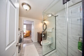 A modern bathroom with a glass shower enclosure, a toilet, and a washing machine. - Watch Deer from a Farm Cottage (Bel Air)