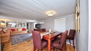 A dining area with a wooden table and chairs, a sofa, and a television in the background. - Watch Deer from a Farm Cottage (Bel Air)