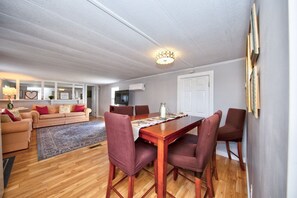 A dining area with a wooden table and chairs, a sofa, and a television in the background. - Watch Deer from a Farm Cottage (Bel Air)