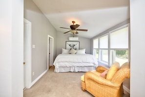 A bedroom with a bed, a ceiling fan, a window, and a wicker chair.
