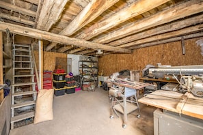 A cluttered workshop with wooden beams, a ladder, and various tools and equipment.