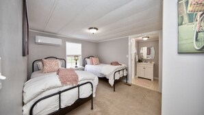 A bedroom with two beds, a window, a bathroom with a mirror, and a wall-mounted air conditioner. - Watch Deer from a Farm Cottage (Bel Air)