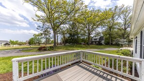 Une terrasse en bois avec une balustrade blanche, entourée d’une pelouse bien entretenue et d’arbres.
