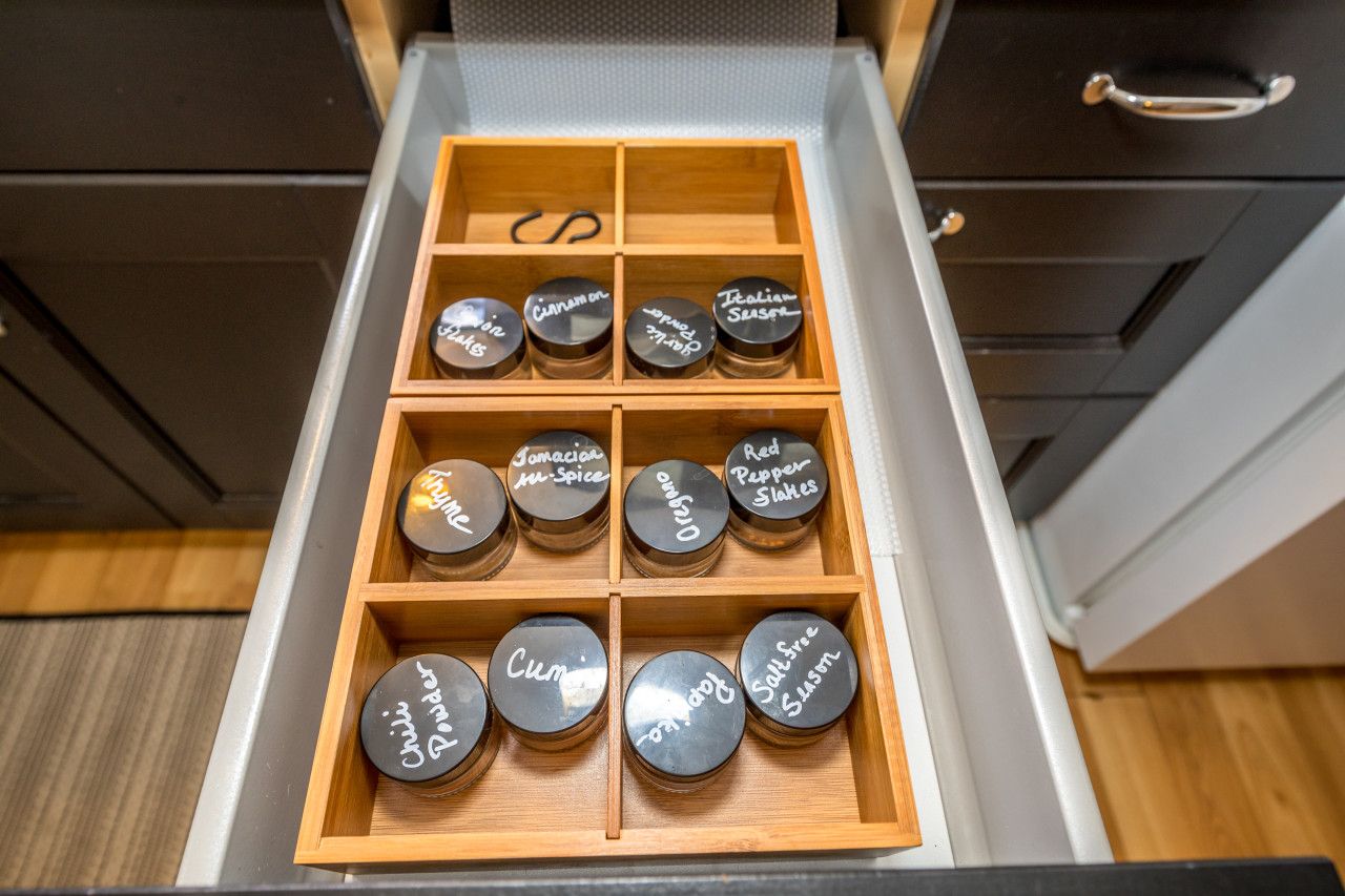 A drawer with multiple compartments containing jars labeled with various spices.