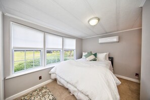 Un dormitorio con un ventanal grande, una cama con ropa blanca, un cabecero y una lámpara en el techo.