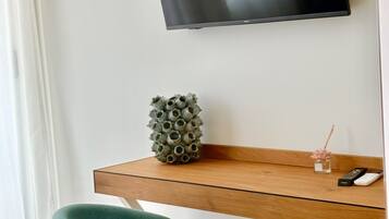 Quarto moderno com televisão de tela plana presa em uma parede branca, uma prateleira de madeira com objetos decorativos e uma cadeira azul-turquesa.