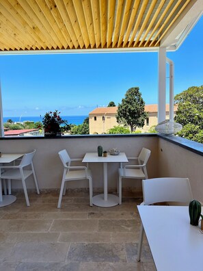 A covered patio with a table and chairs, a cactus, and a view of the ocean and buildings. - Kairos Tropea (Tropea)