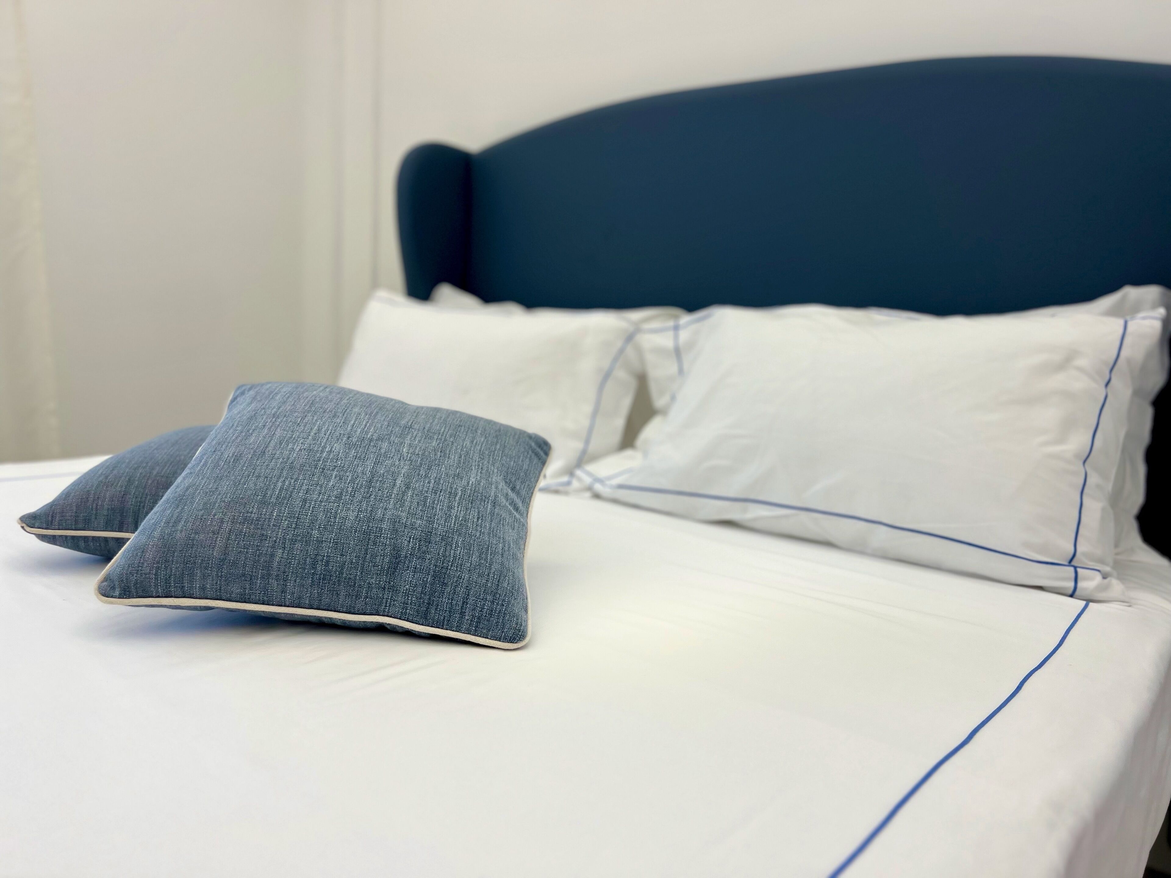 A bed with a dark headboard, white bedding, and two grey pillows.
